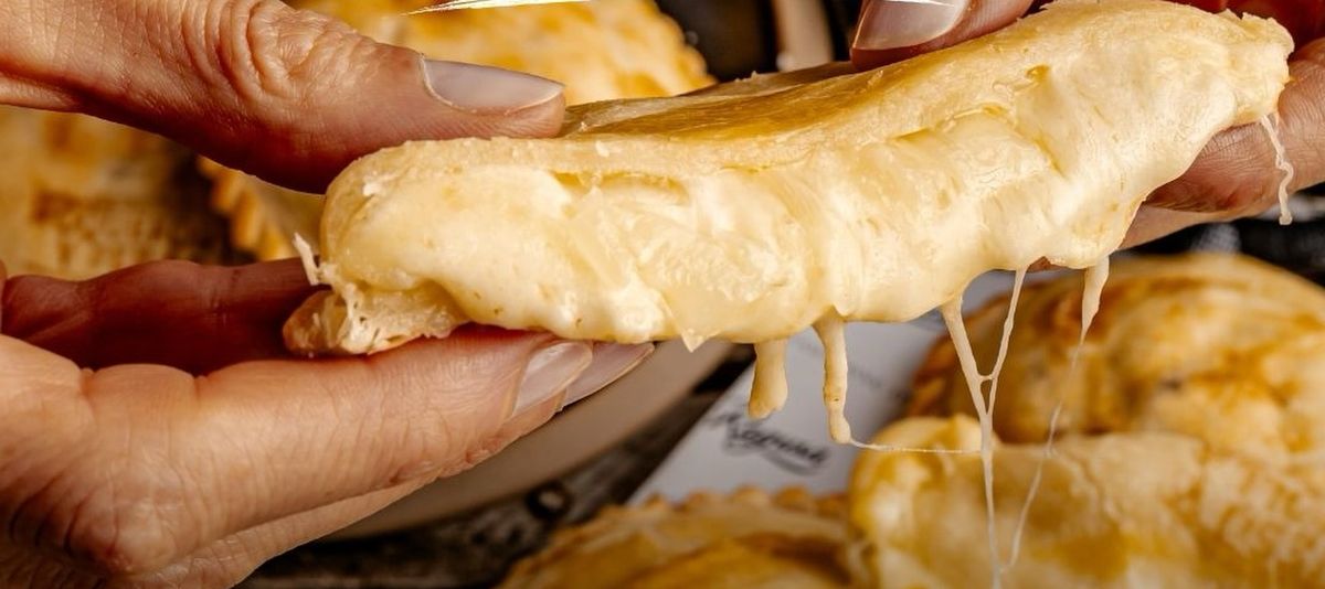 Empanada de queso abierta con las manos, con el queso derritiéndose.